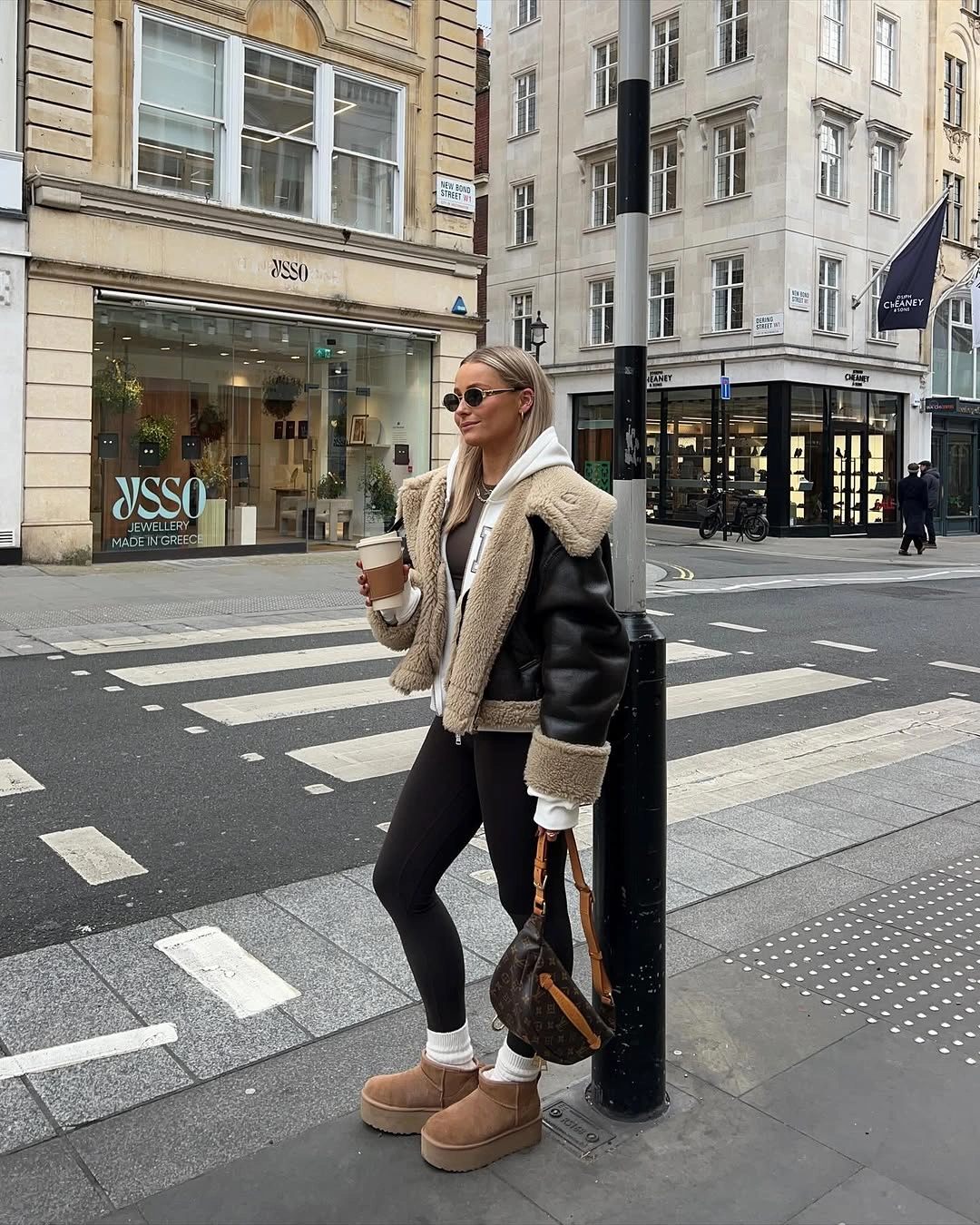 Black jacket with cream collar, gray hoodie, slim black pants, and tan ankle boots.