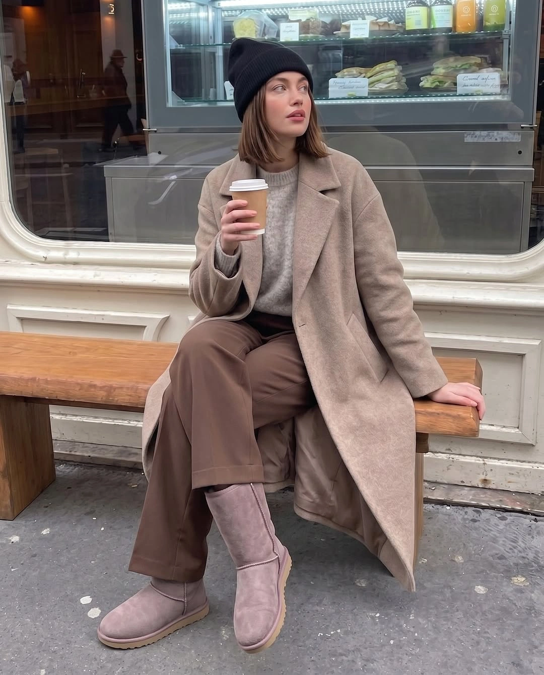 Long taupe coat, black beanie, gray sweater, loose brown trousers, and muted pink boots.