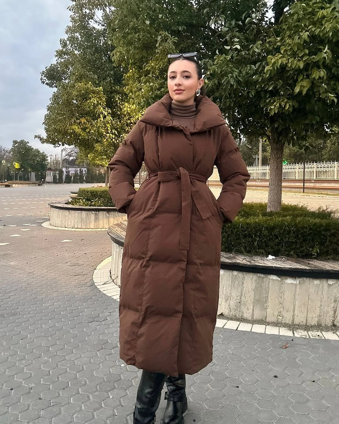 Belted brown puffer with tall collar, brown turtleneck, black knee-high boots, and sunglasses on head.