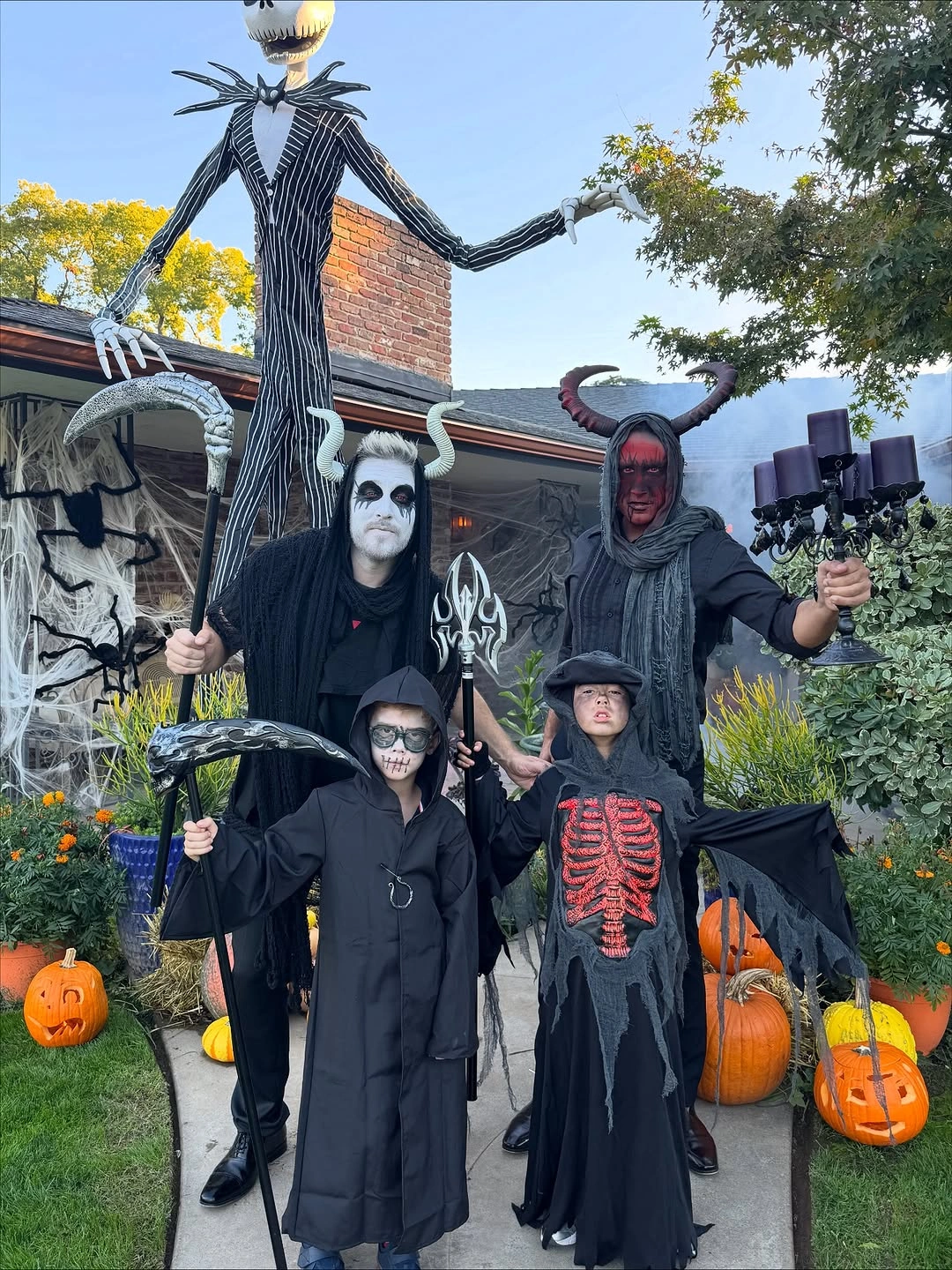 Family in black hooded reaper and skeleton-print Halloween costumes on a lawn