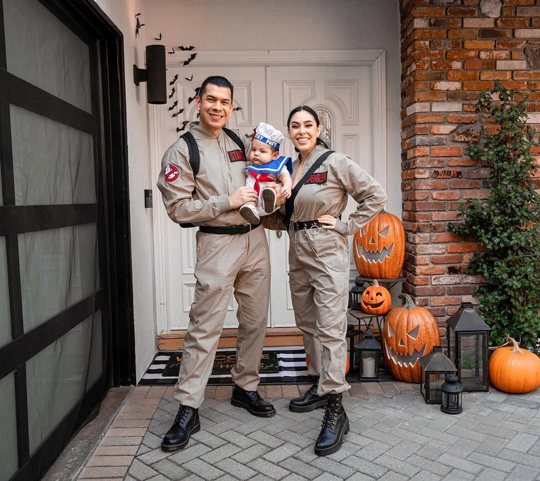 Family in beige utility coveralls with black backpacks and Halloween pumpkin buckets