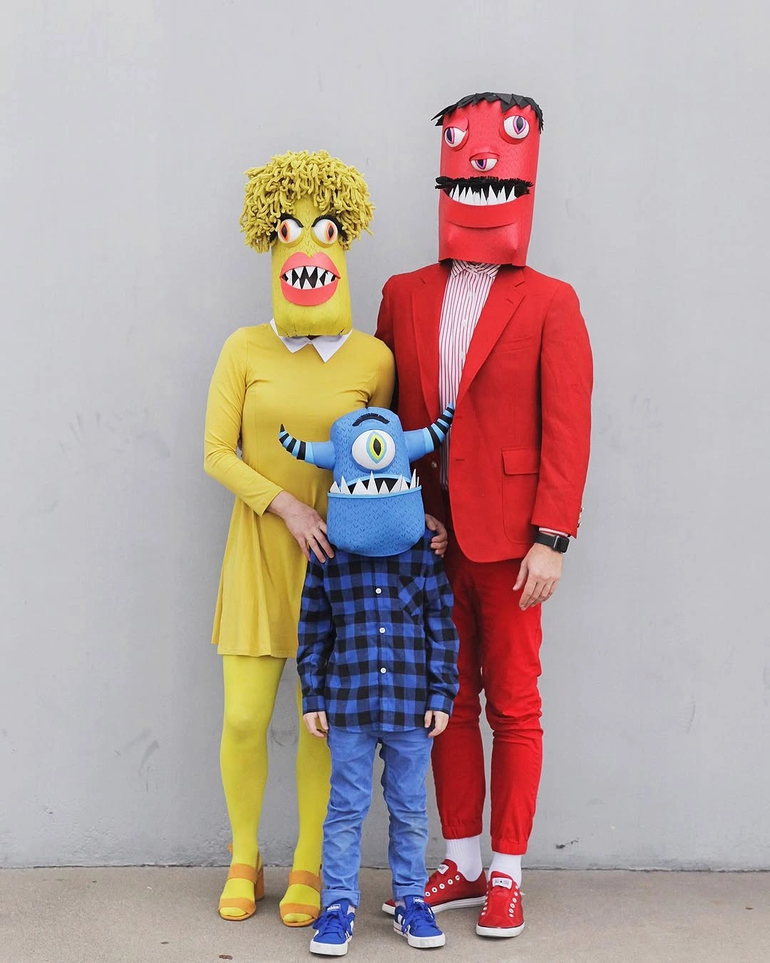 Adults in yellow and red monster headpieces with a child in a plaid Halloween outfit
