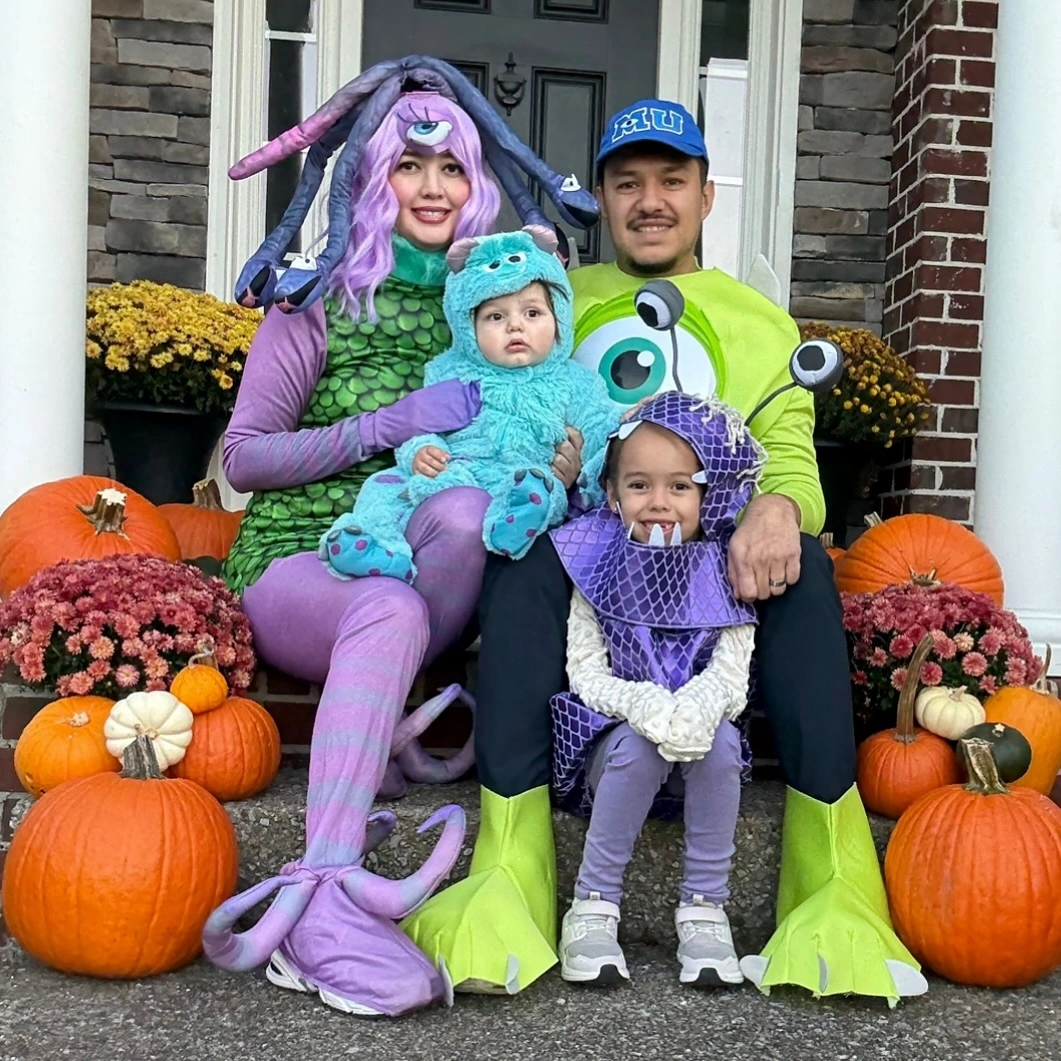 Family in purple green and blue playful monster Halloween costumes by pumpkins