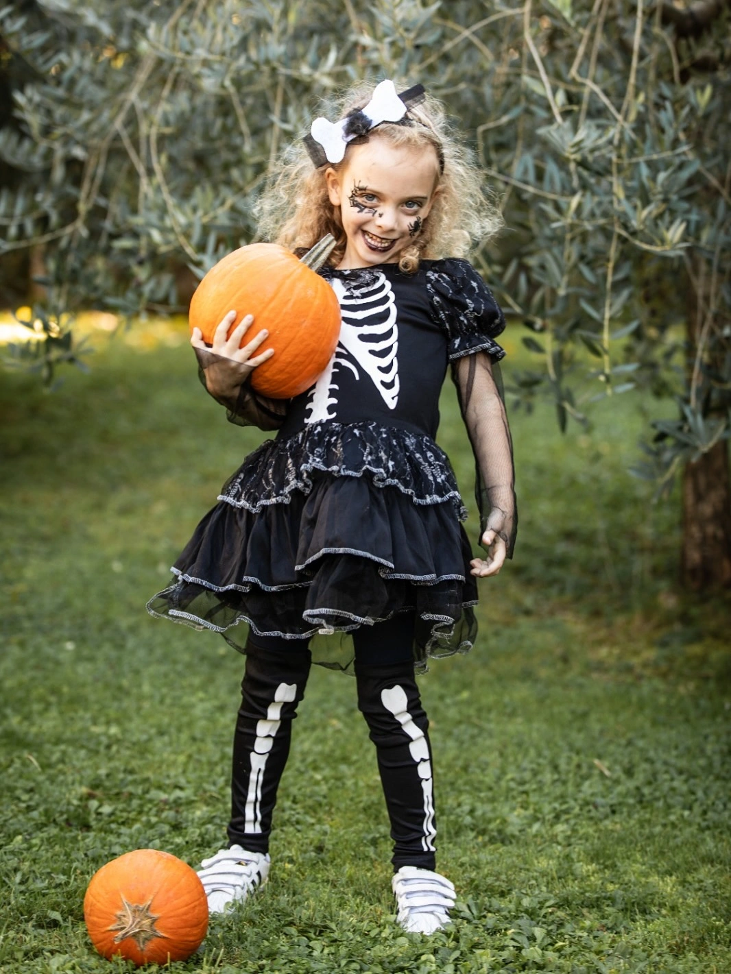 Girl in black skeleton-print dress with black white striped leggings and skull bow