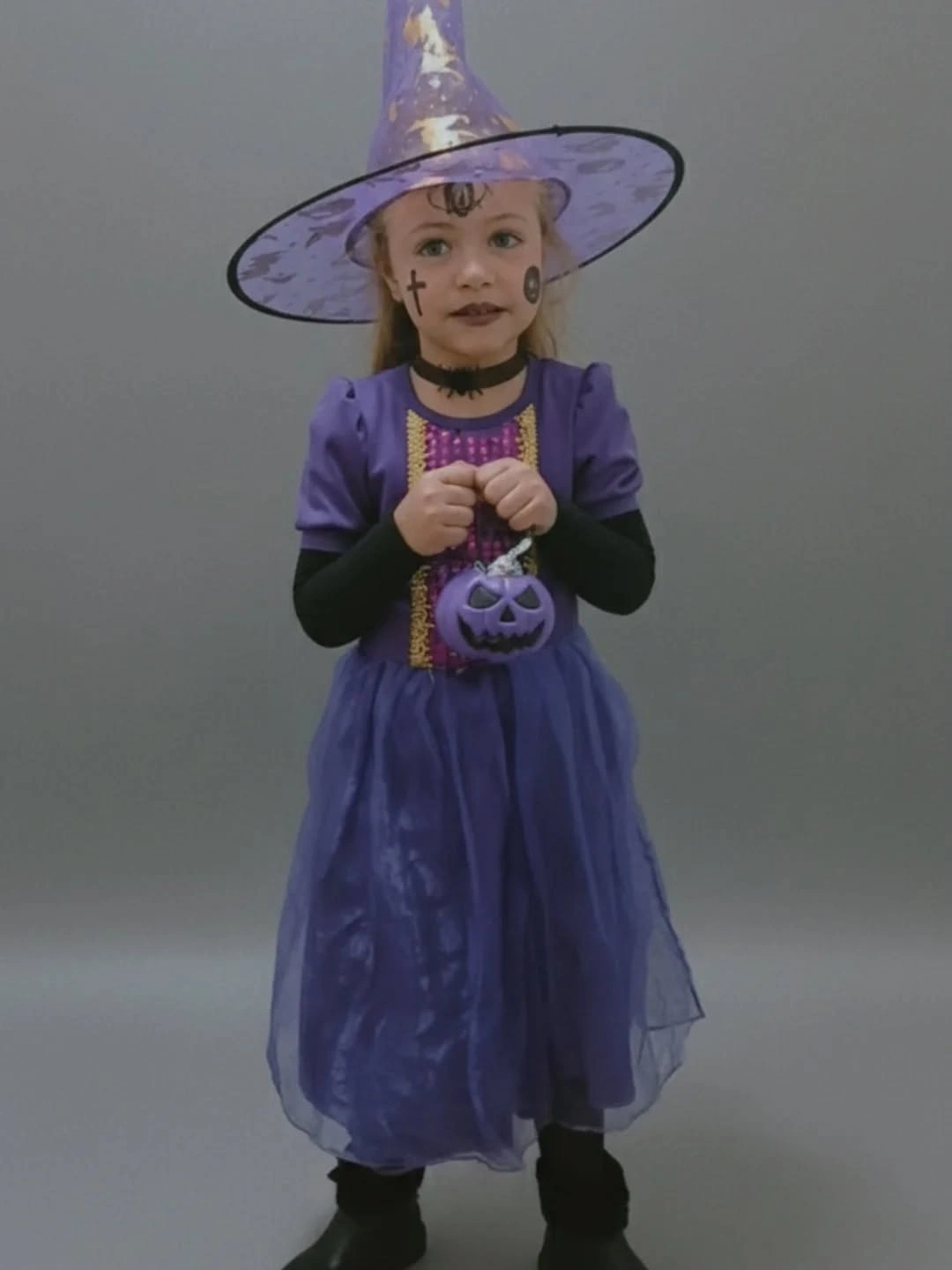 Girl in flowing purple witch Halloween costume with pointed hat and pumpkin bag
