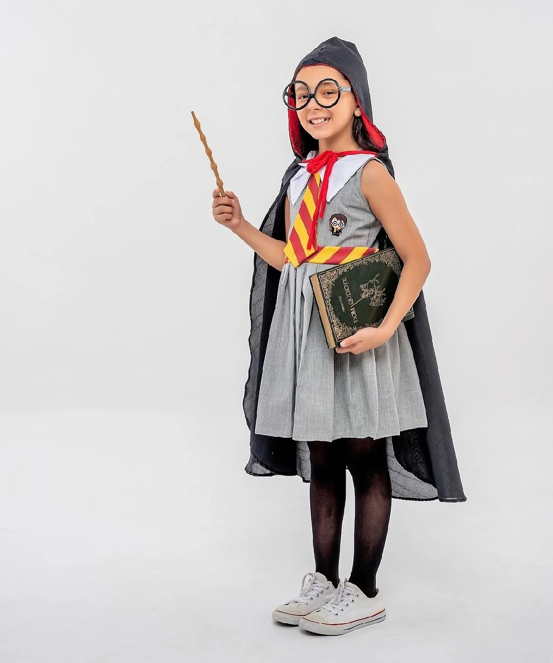 Girl in dark cape school costume with gray pleated skirt round glasses book and wand