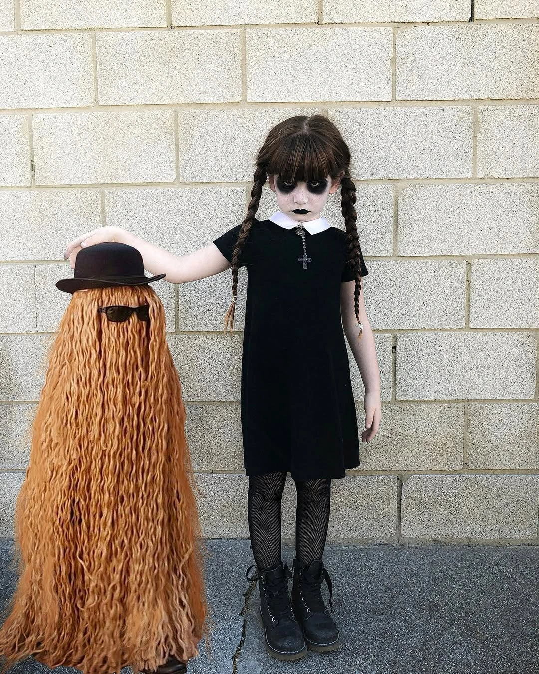 Girl in black collared gothic dress with braids beside tall furry brown costume