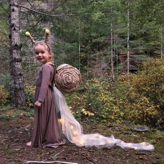 Girl in brown woodland creature costume with spiral shell antennae and glowing gauzy trail