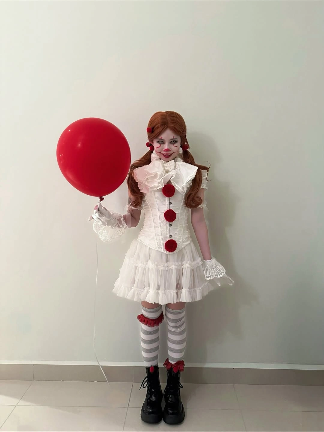 Girl in white ruffled clown-inspired Halloween dress with red pom-poms and striped socks
