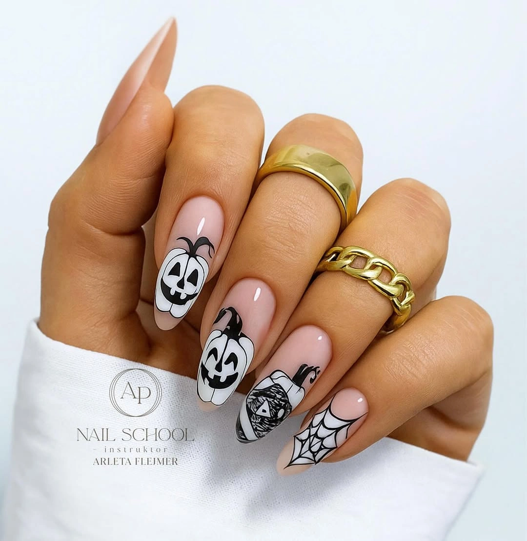 Medium nude almond nails with black white skull faces web and orange Halloween accents