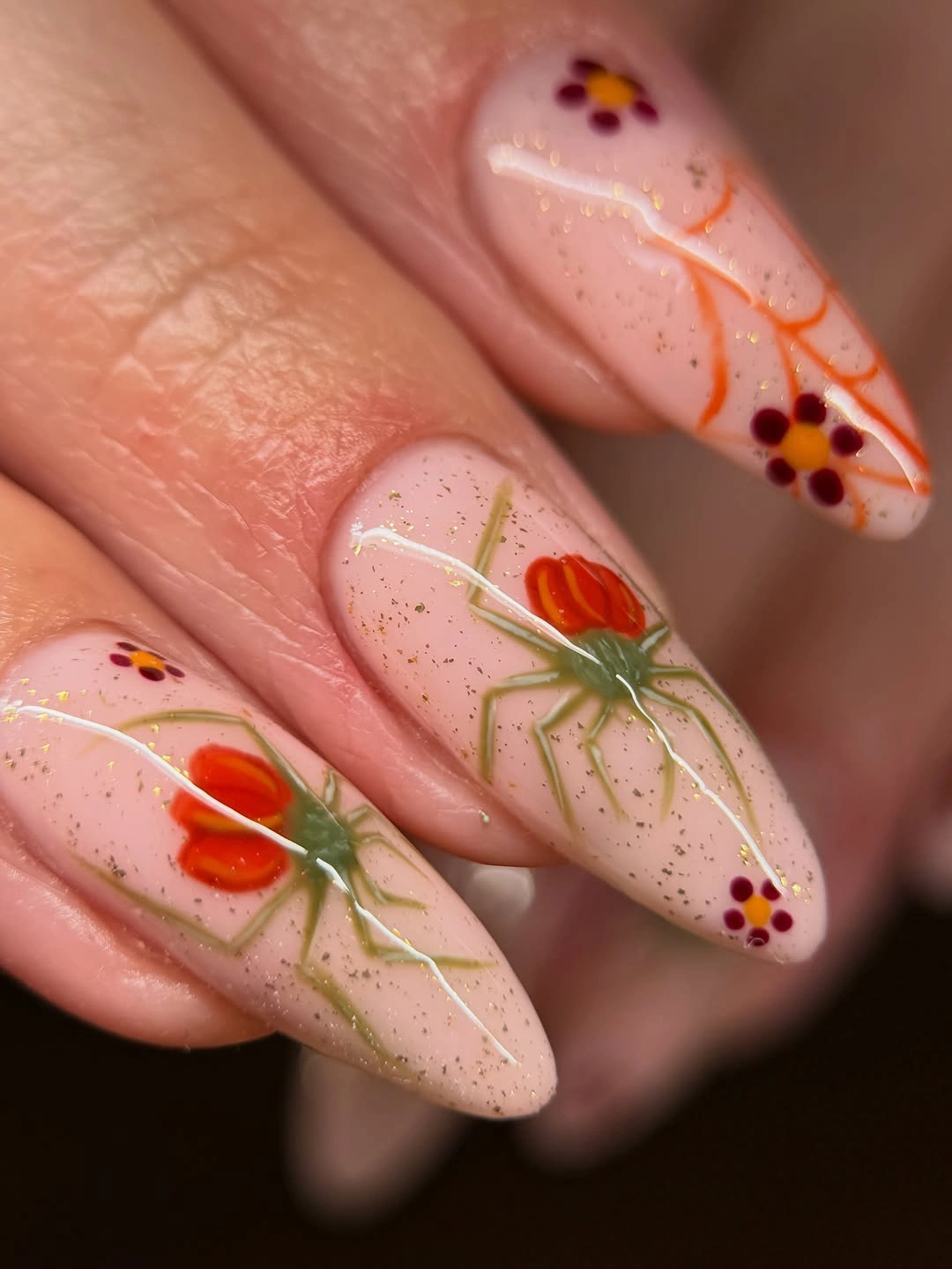 Sheer nude almond nails with orange pumpkins green vines and tiny berry dots