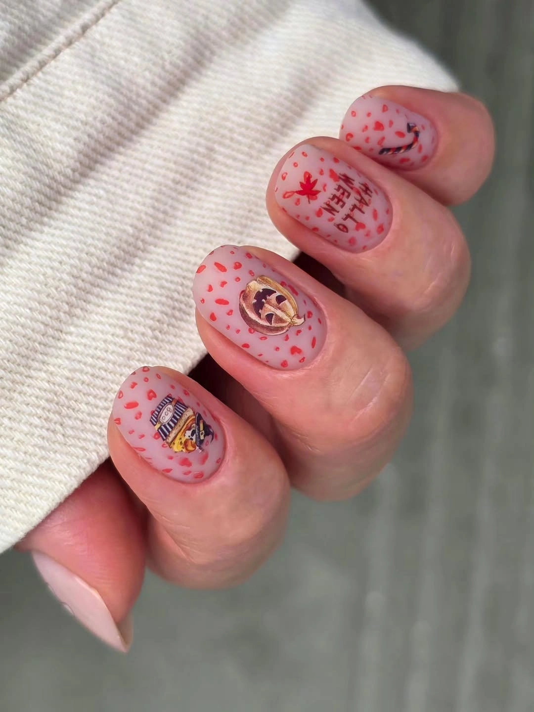 Short pink rounded nails with red speckles tiny framed Halloween art and pumpkin