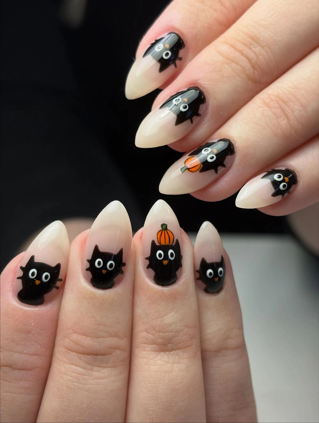 Milky almond nails with black cat faces and small orange pumpkin accents