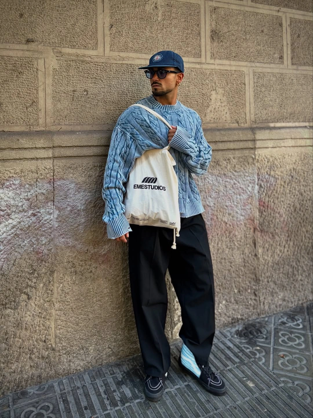 Blue patterned sweater black wide trousers blue cap and cream tote