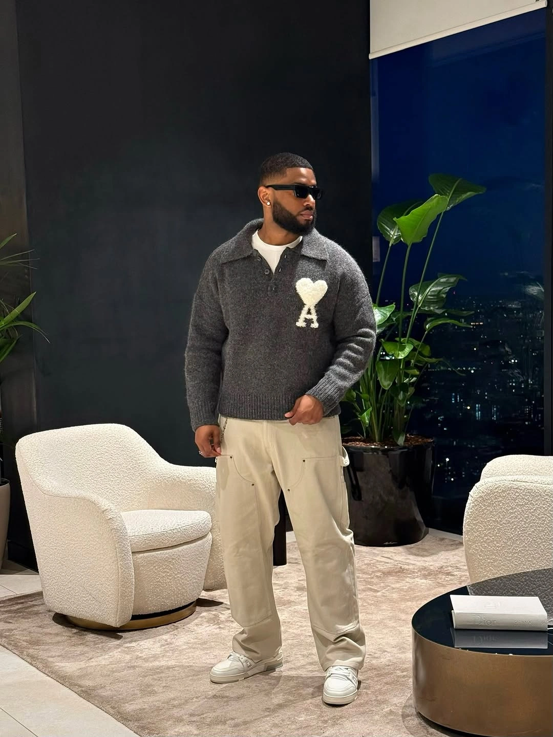 Gray graphic sweater cream trousers and white sneakers in a neutral room