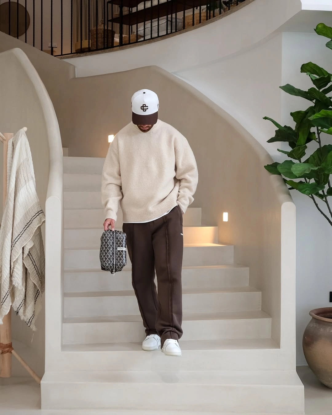 Cream sweatshirt brown trousers white cap sneakers and small patterned bag