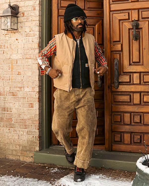 Tan utility vest layered over plaid shirt and brown trousers