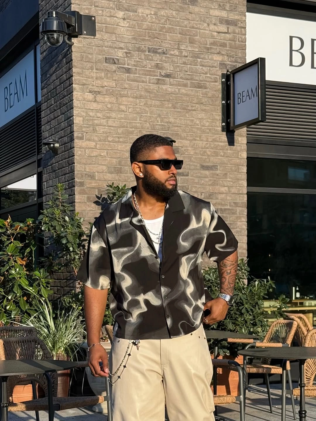 Black patterned short-sleeve shirt with cream trousers and sunglasses