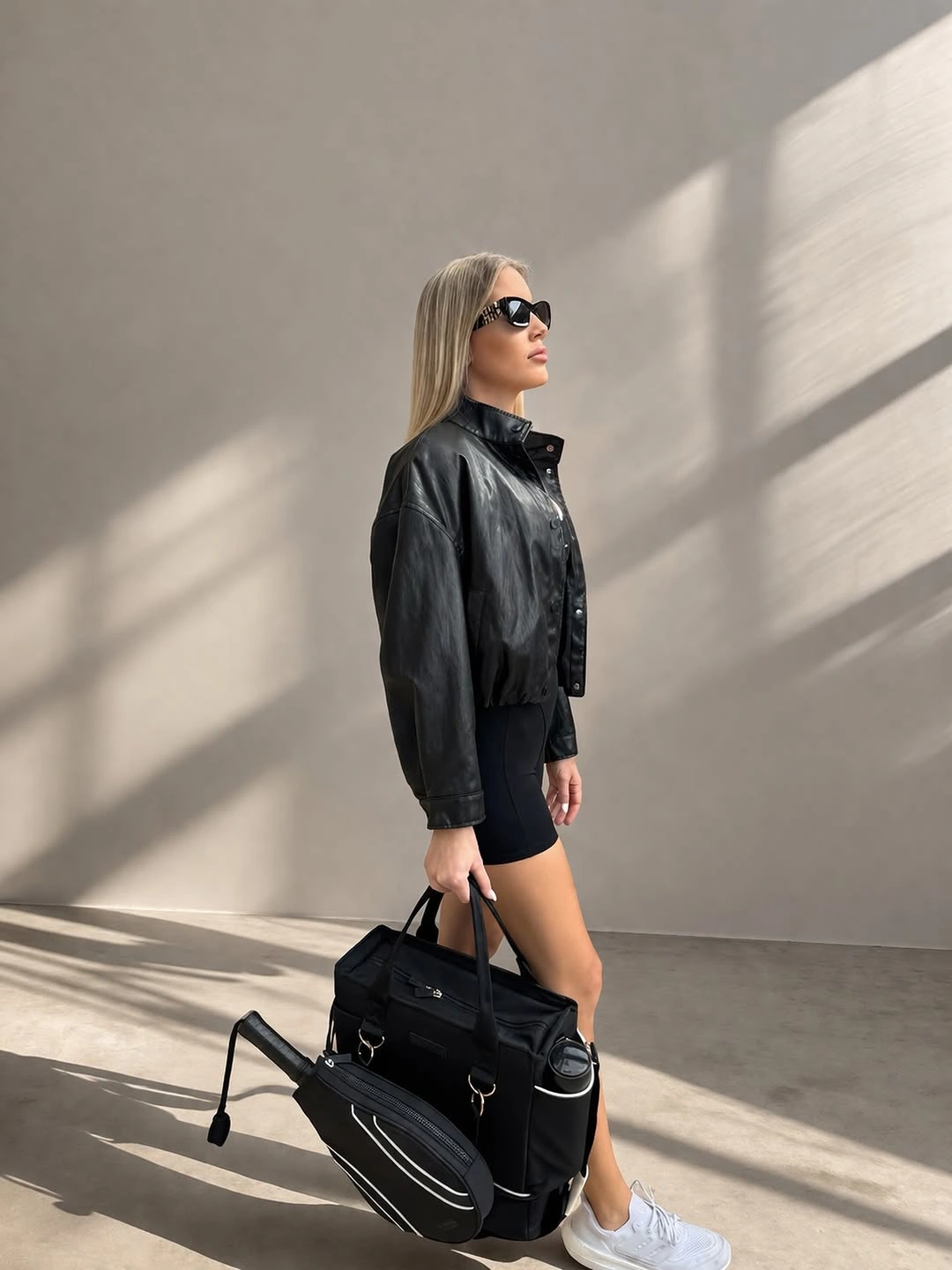 Black jacket and shorts with white sneakers and padel racket bag