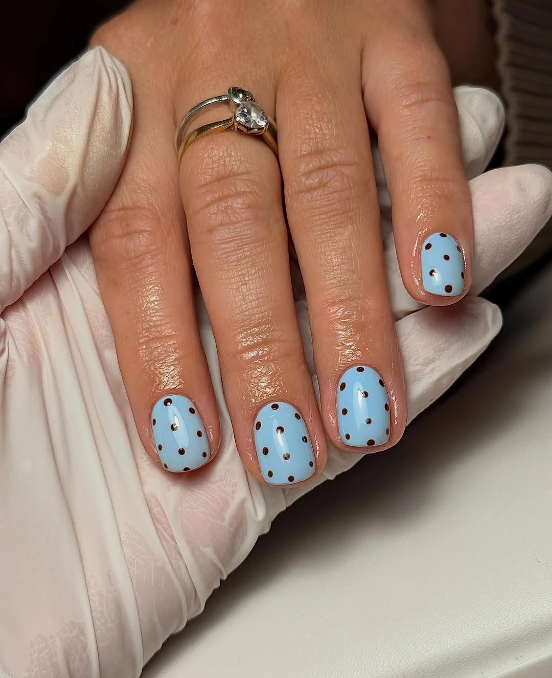 Short rounded light blue nails with evenly spaced black dots and pale pink accent nail