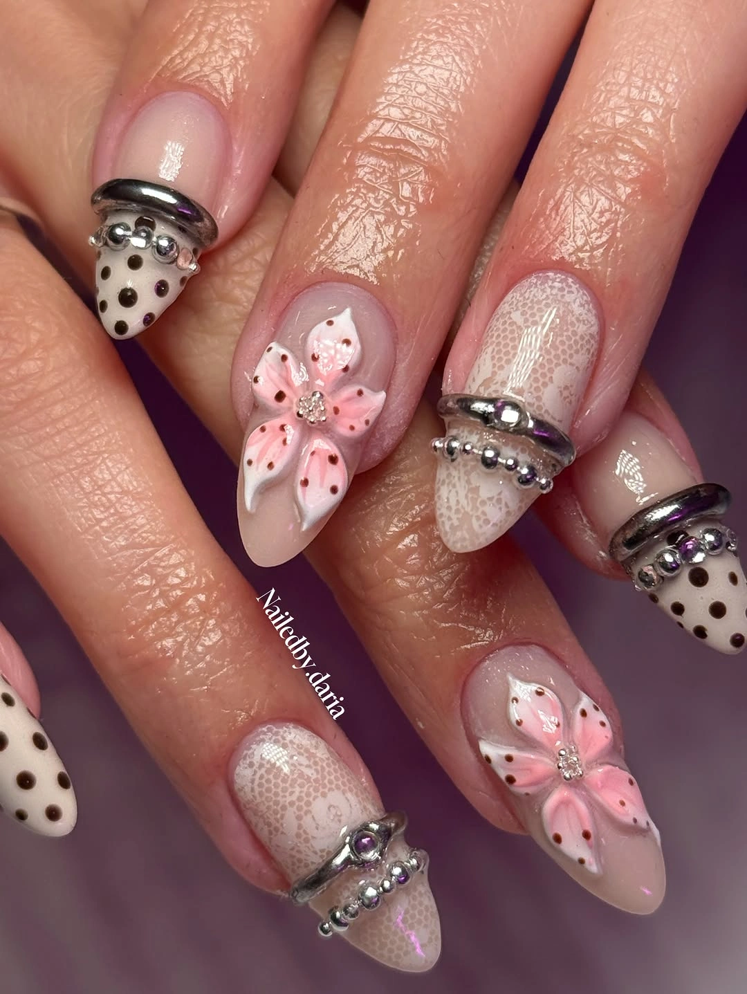 Long pale nails with black dotted white tips, large pink floral accents, and translucent pale detail