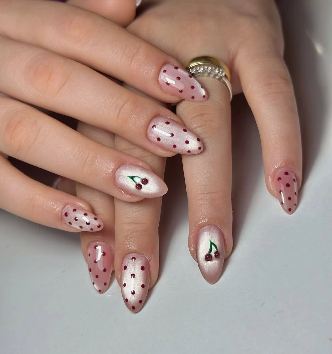 Pale pink nails with red dots, red French-style edge, white accent nail, and small green detail
