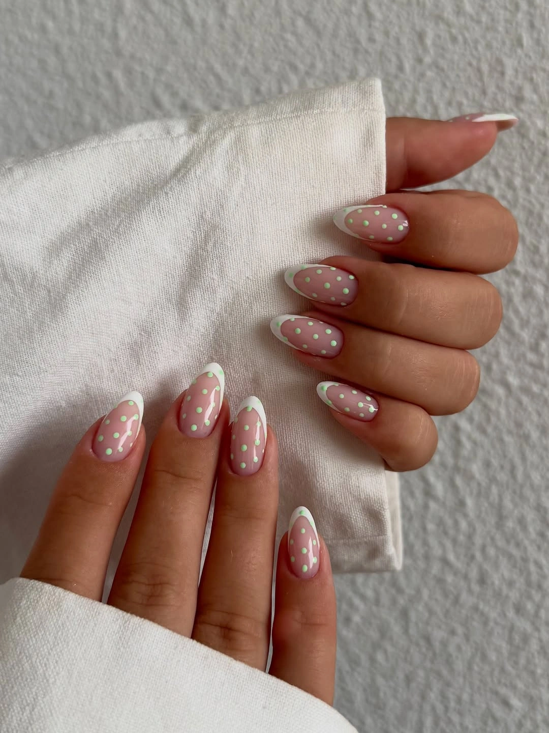 Warm nude almond nails with lightly spaced white dots and soft pale French-style tips