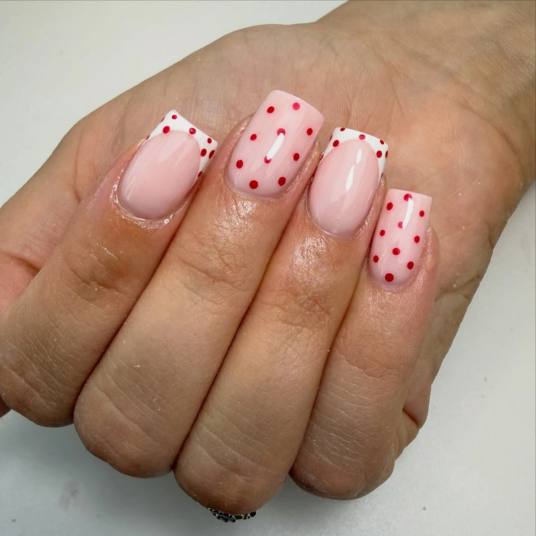 Nude nails with black white dotted French tips, tiny multicolor dots, and small gold bead-like accents