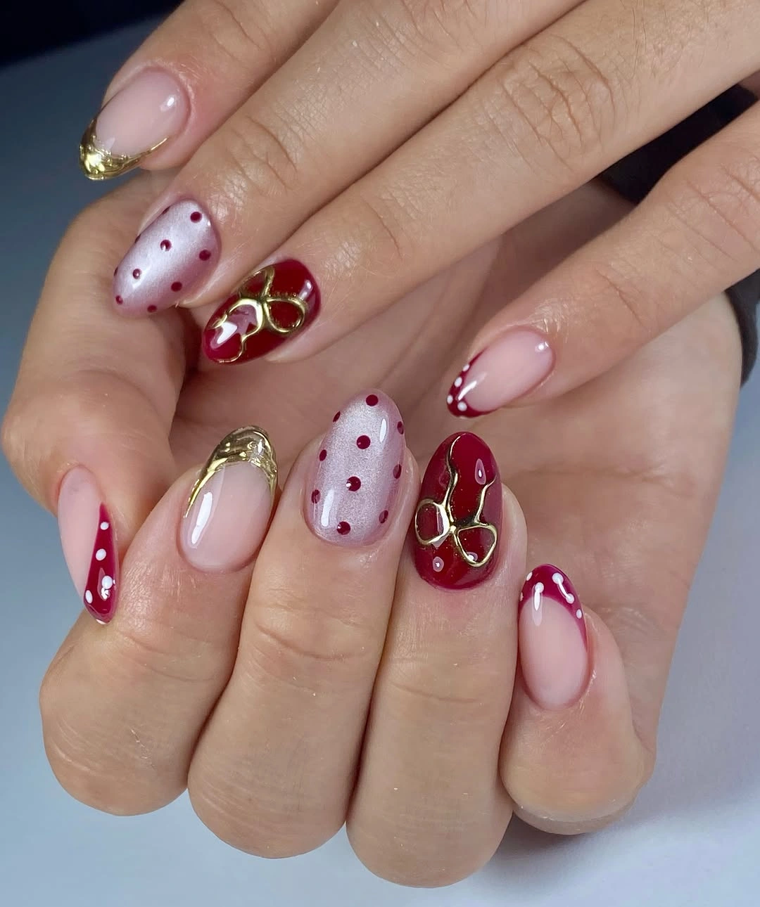 Pale pink nails with red dots, deep red accents, white tips, and curved gold-like details