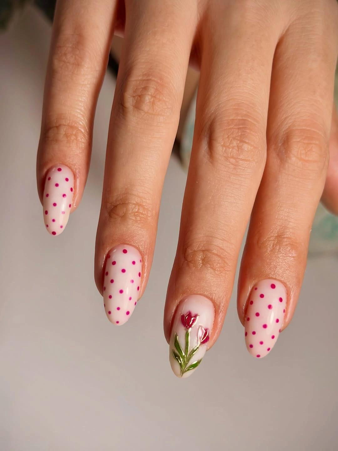 Pale pink almond nails with small red dots and one red floral accent nail