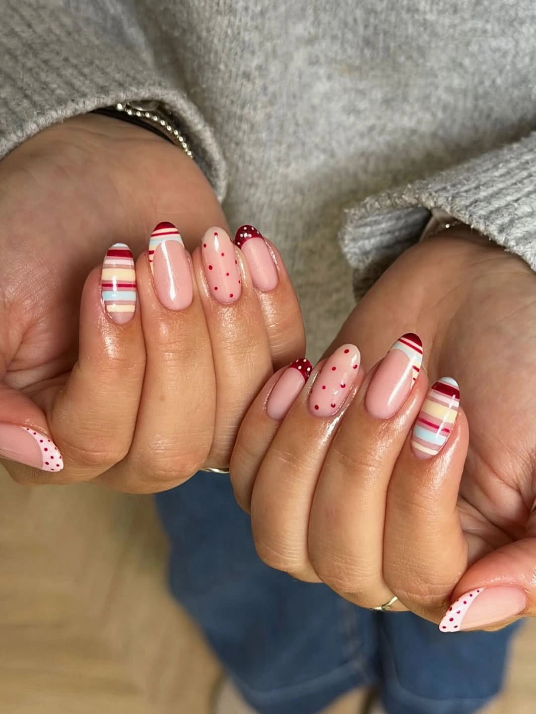 Pale pink nails with white tips, red stripes, red dots, and curved red accent edges