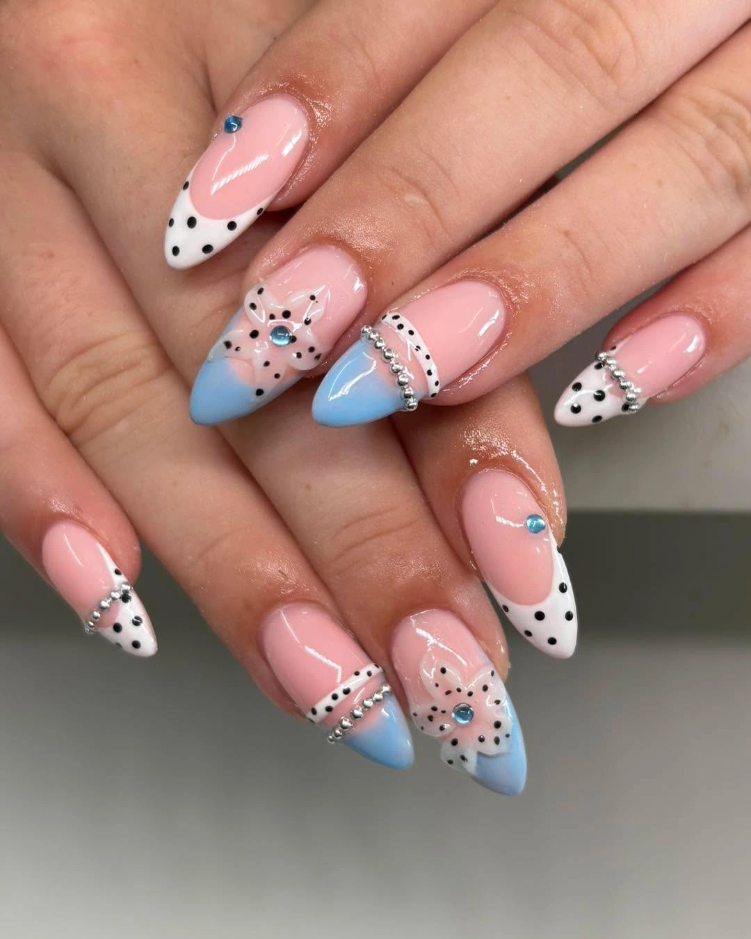 Pale pink almond nails with black white dotted tips and soft sky blue accent sections