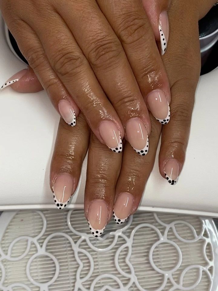 Short nude almond nails with tiny black dots along small white French tips