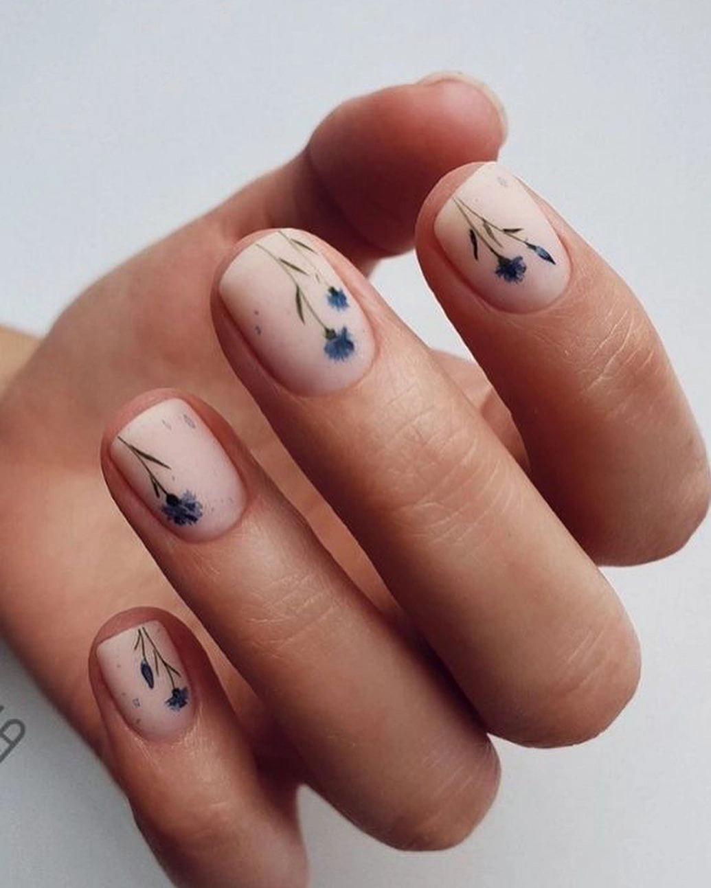 Short nude-pink nails with delicate blue floral stems