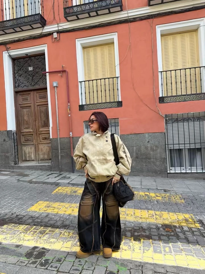 Tan utility outfit with green top, patterned front crossbody bag, tinted glasses, and relaxed trousers