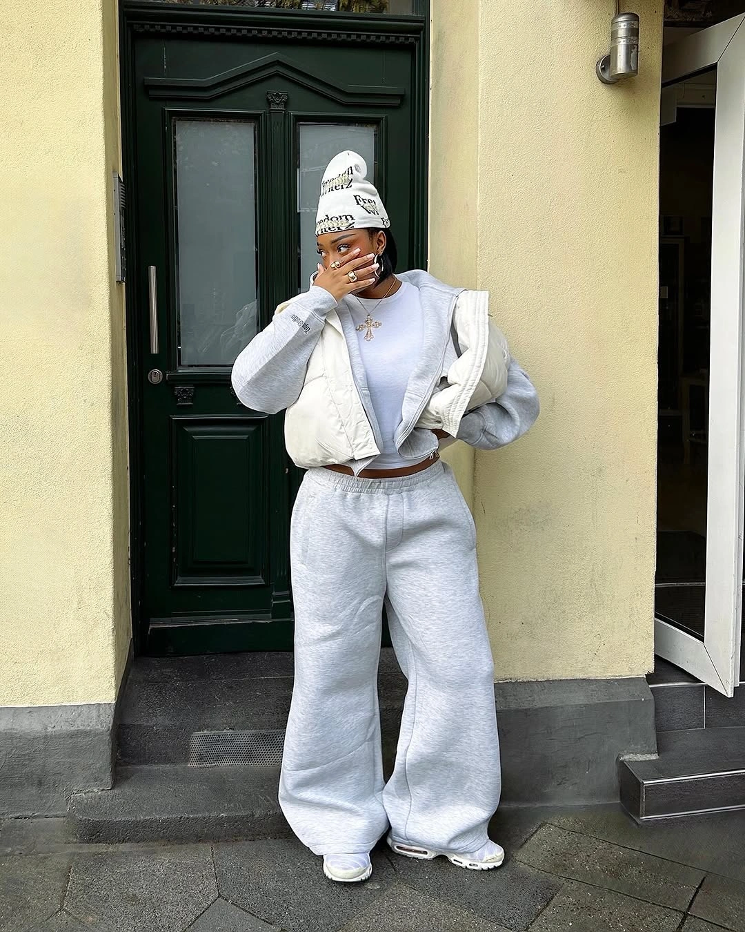 Cropped white puffer vest over gray hoodie and loose gray sweatpants with white beanie and shoes