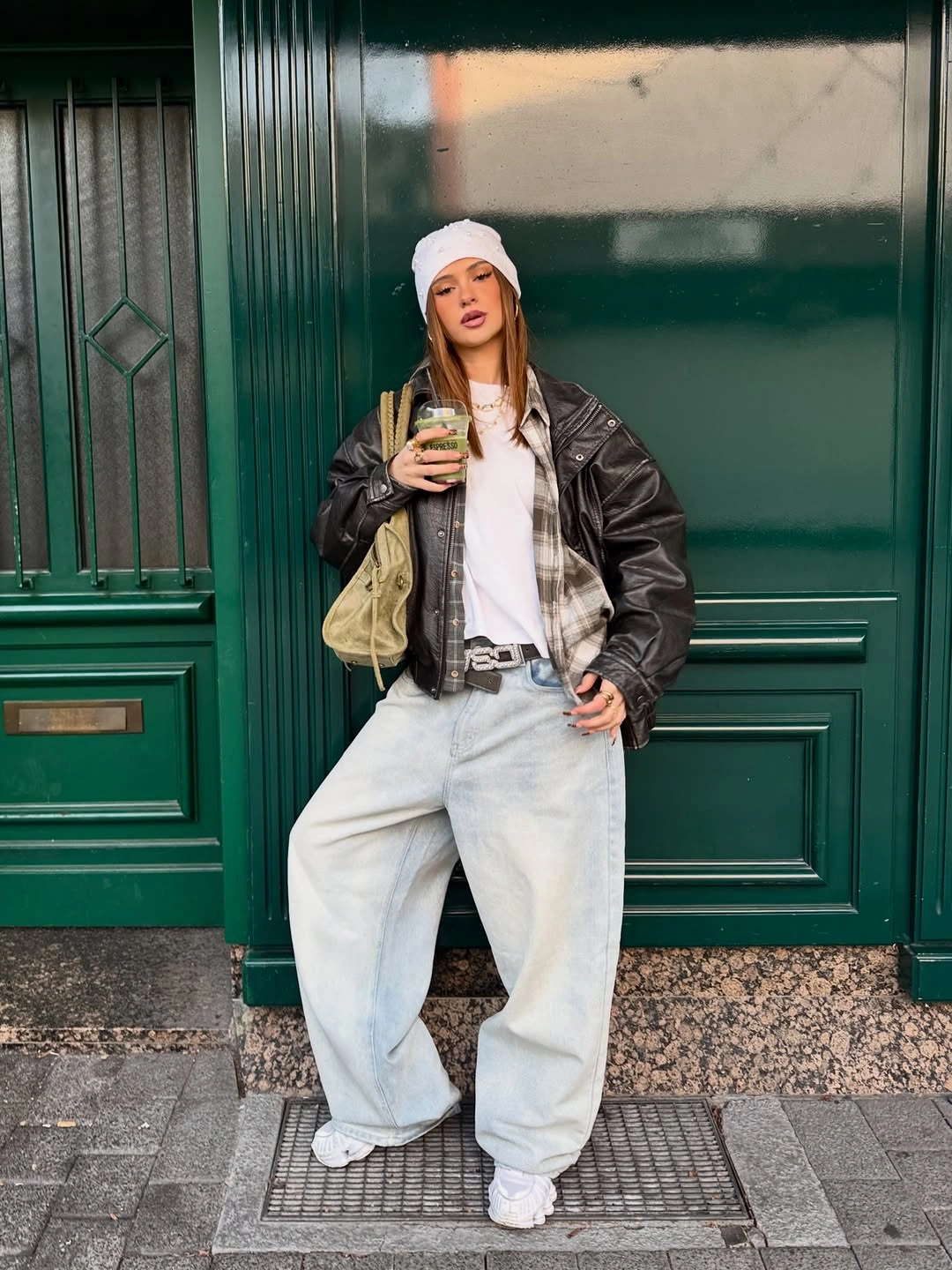 Black shiny bomber with white T-shirt, pale wide jeans, white beanie, white sneakers, and small metallic bag