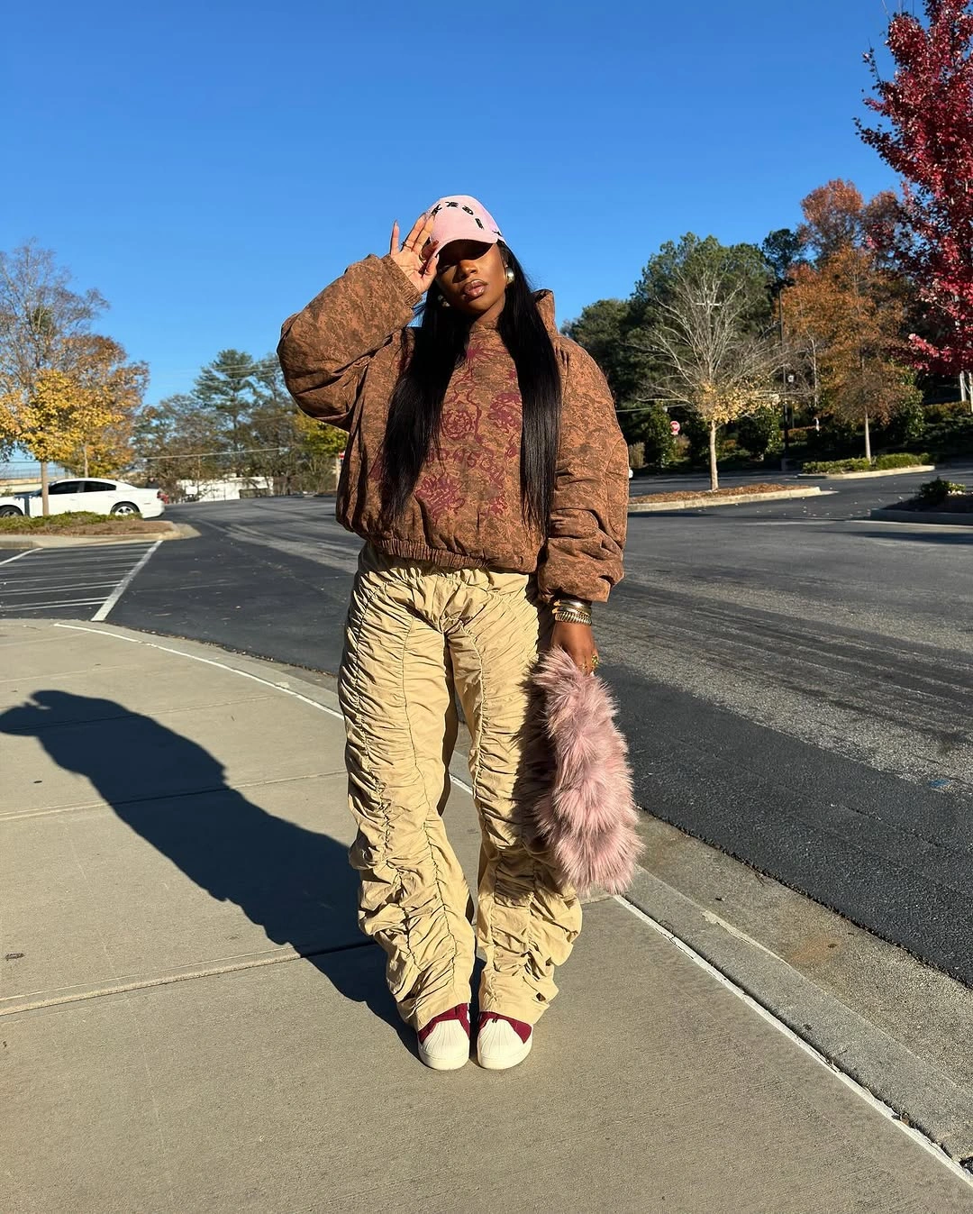 Brown textured puffer jacket with tan cargo pants, pale pink cap, pink fuzzy bag, and light shoes