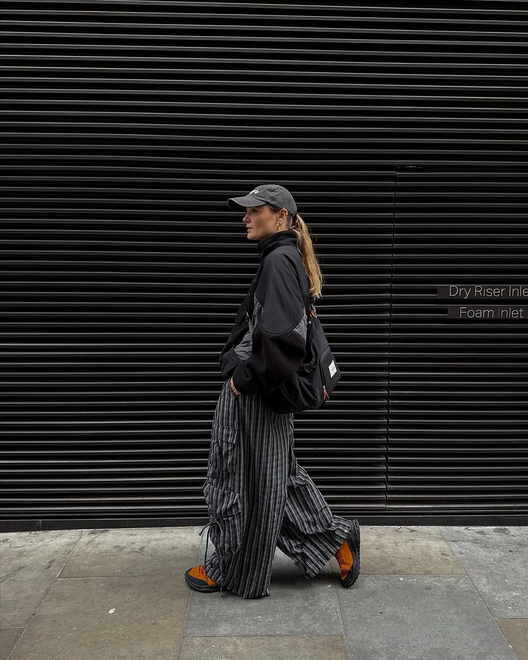 Black cap and jacket with vertically striped wide trousers, backpack, and orange accented shoes