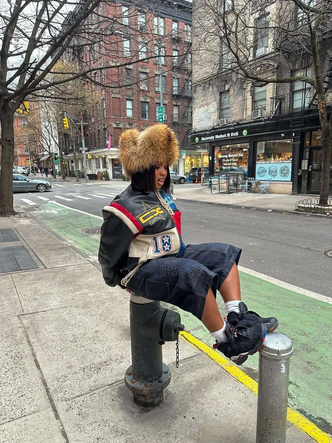 Large brown fuzzy hat with dark sporty jacket, short denim layer, tall black boots, and black bag