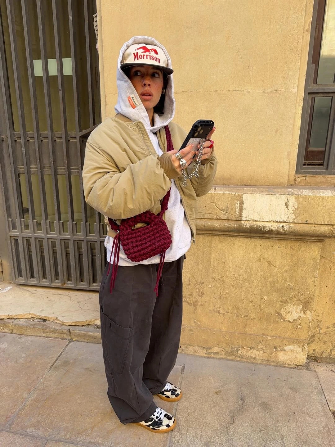 Cream puffer jacket and white hoodie with loose dark trousers, red crossbody, and patterned shoes