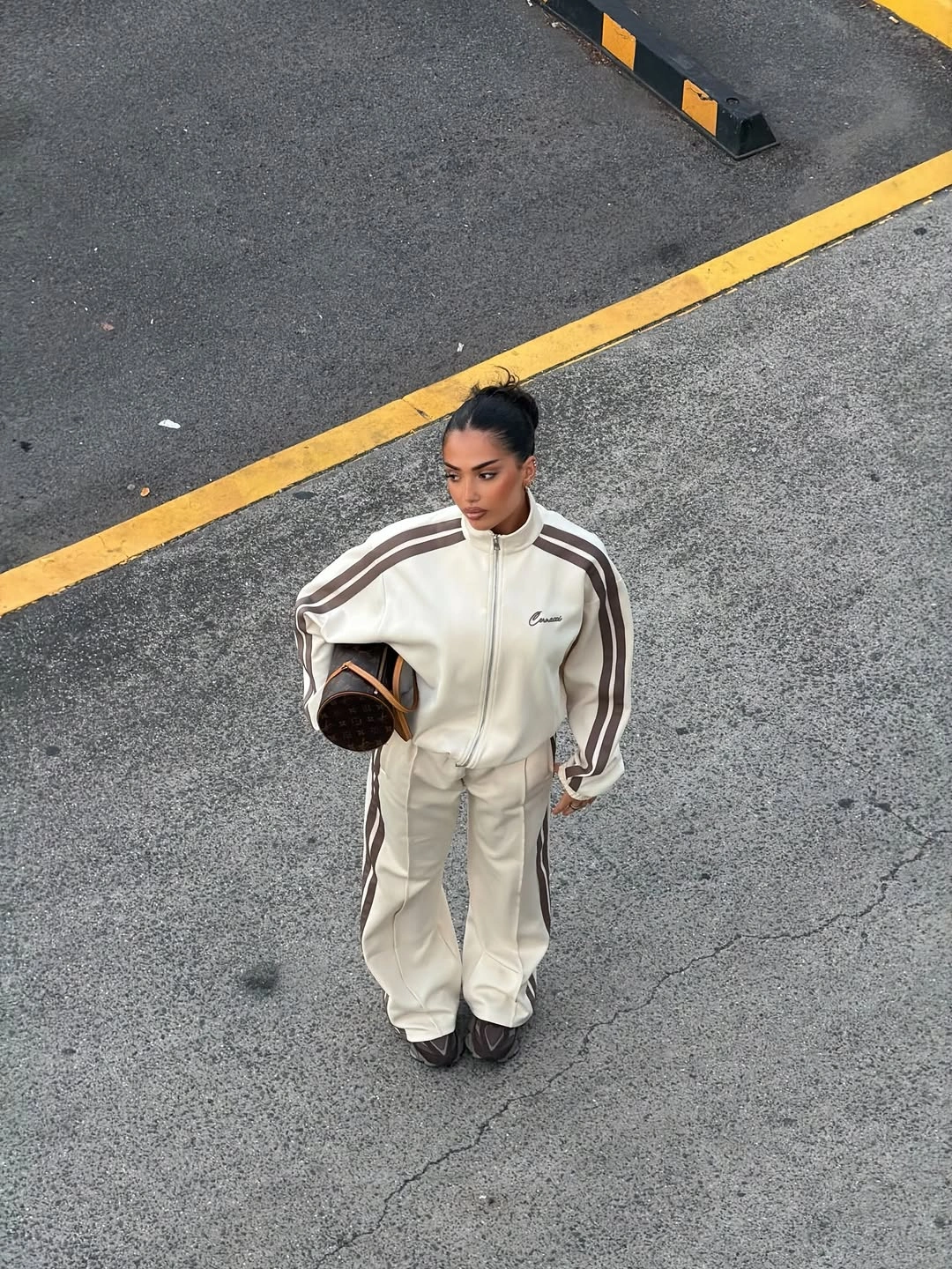 White striped track jacket with loose white pants, dark cap, and dark shoulder bag
