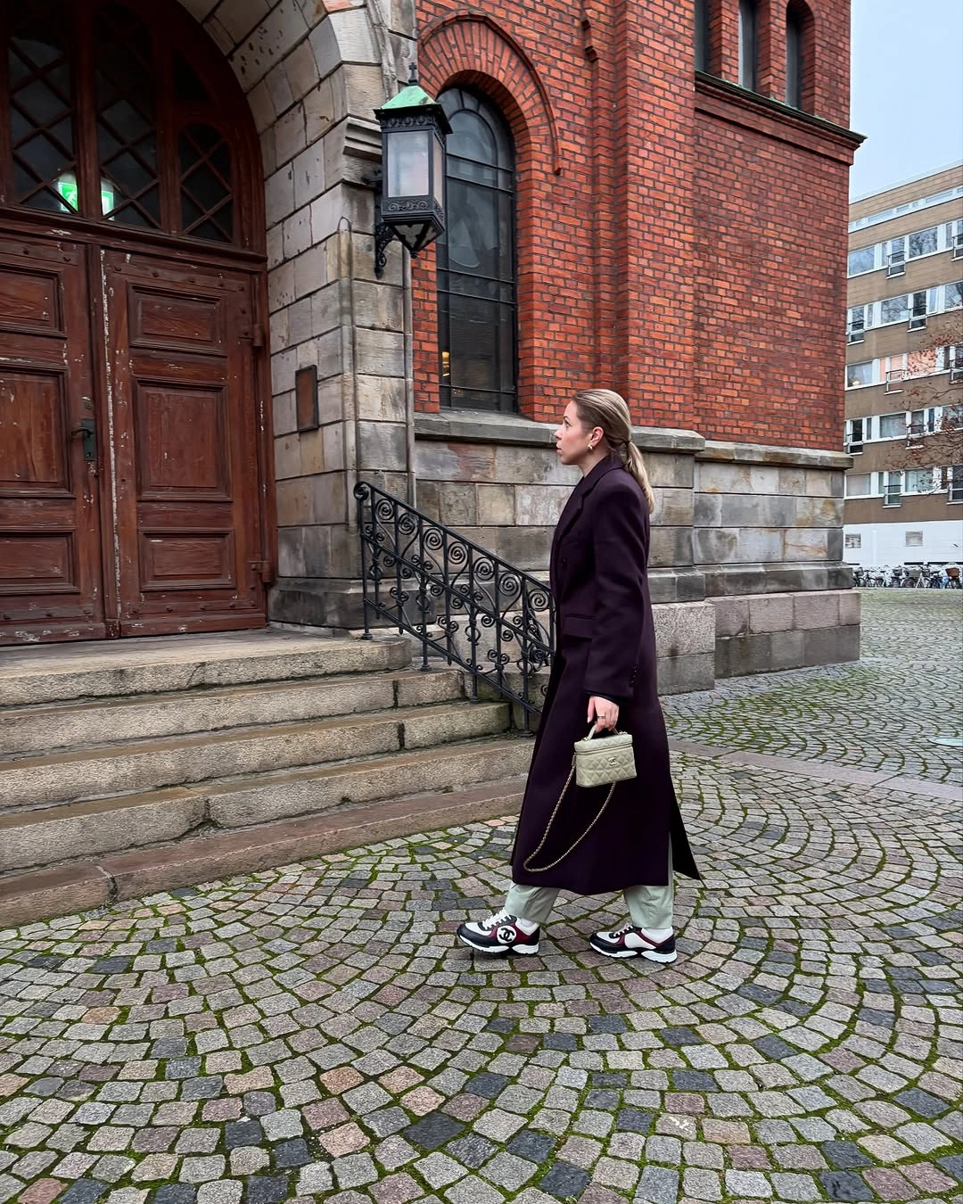 Deep plum long coat with pale trousers and chunky sneakers