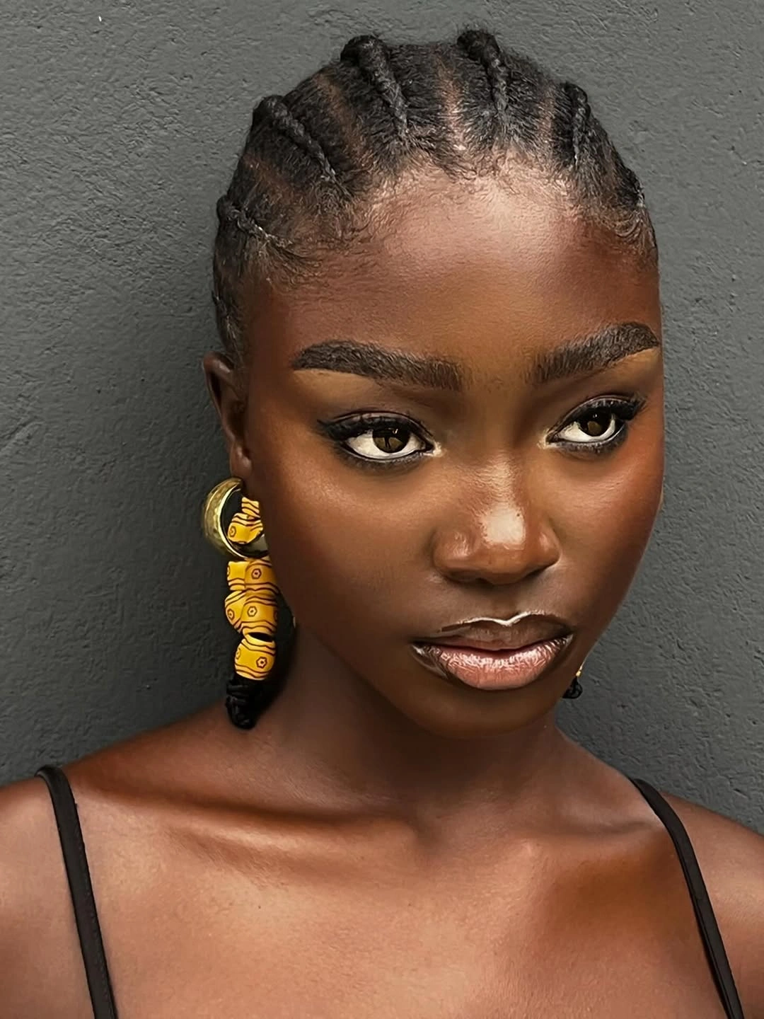 Raised braids with clean parting against a gray wall