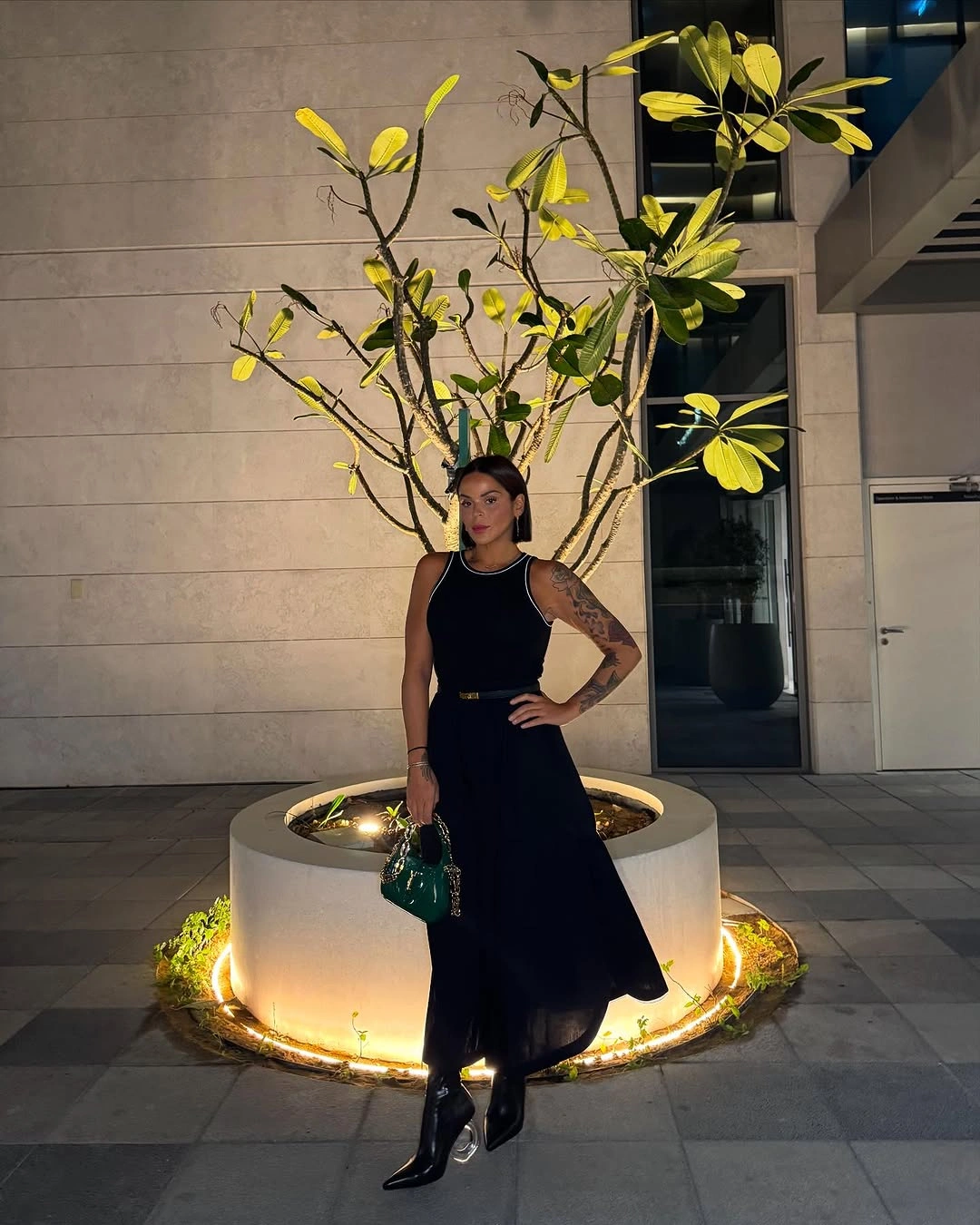 Black sleeveless dress with glossy boots and green handbag