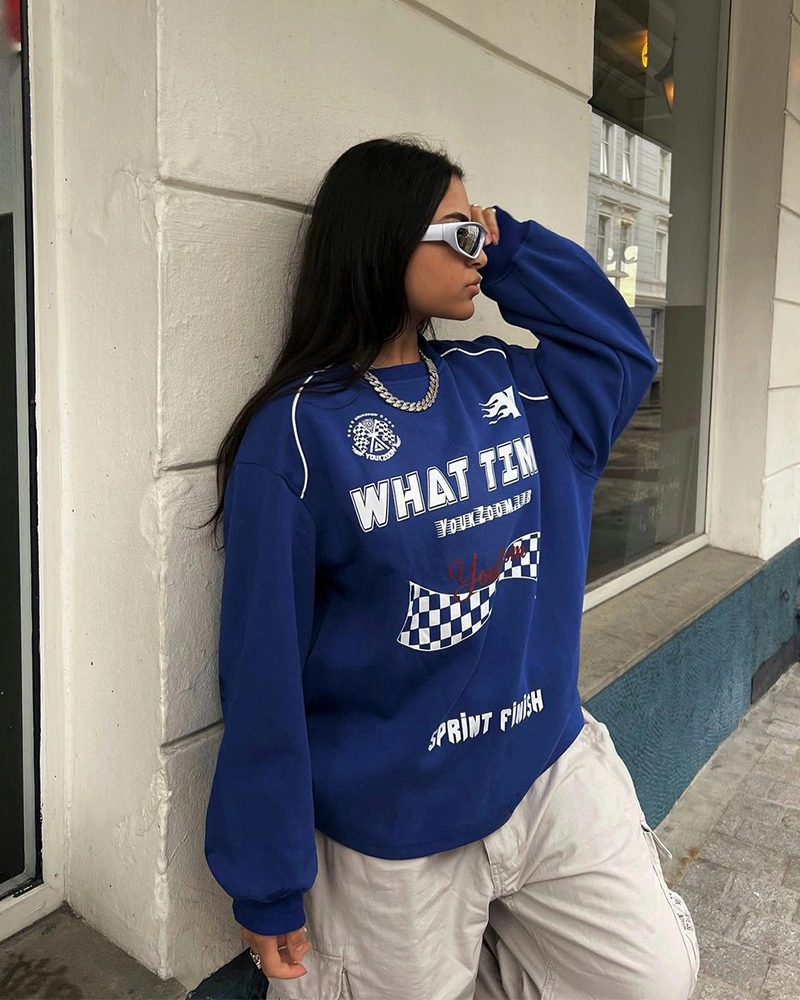 Blue graphic sweatshirt with pale trousers and white sunglasses