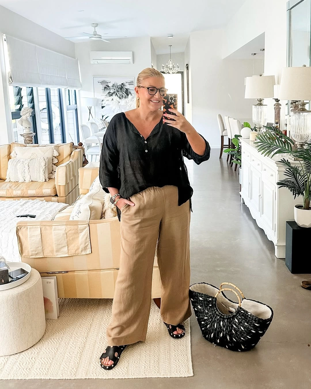 Black loose blouse with beige wide trousers and woven tote
