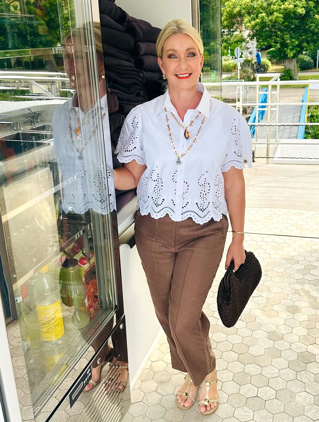 White eyelet shirt with brown trousers and woven clutch