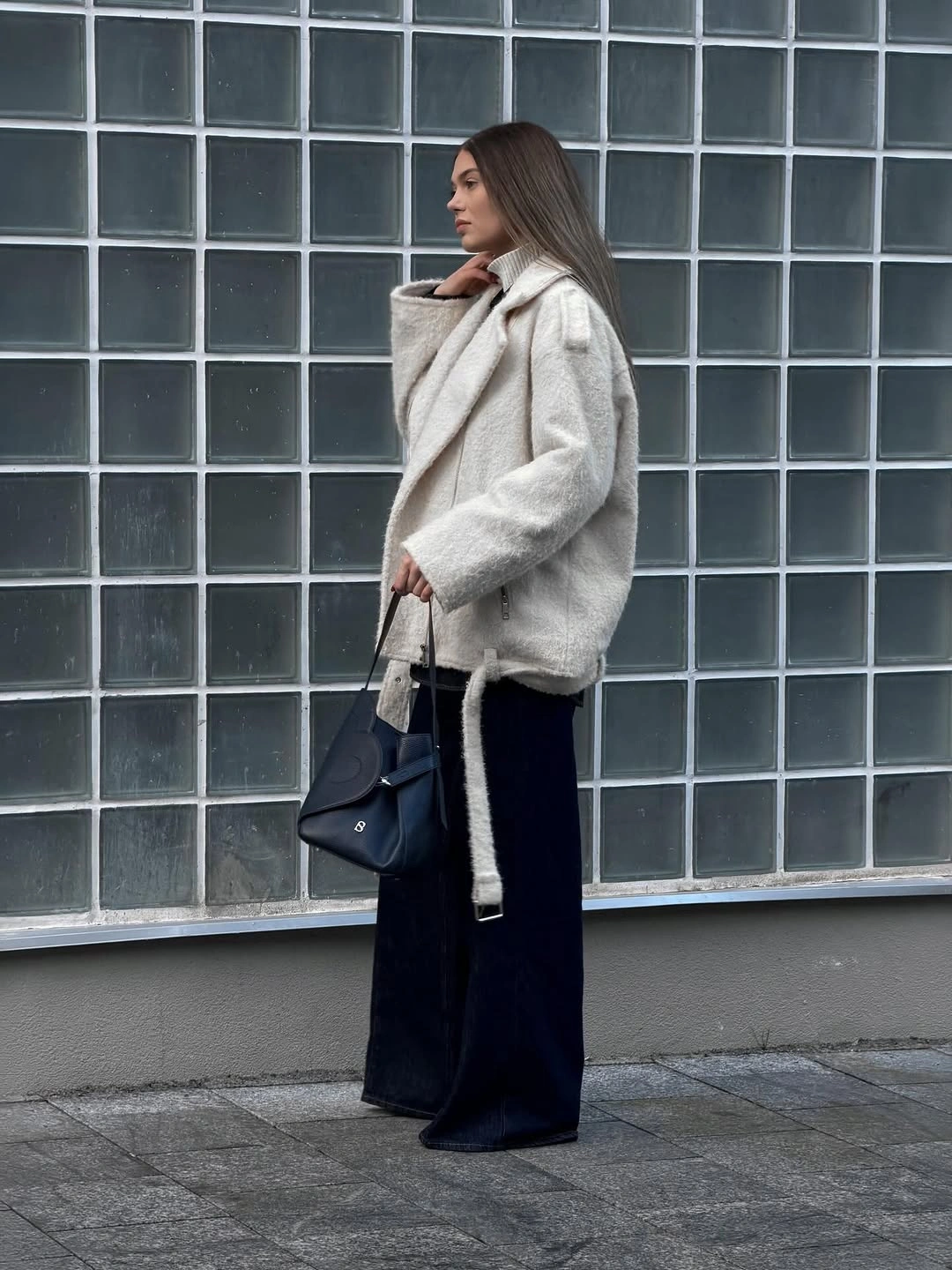 Cream fuzzy-looking coat with black wide trousers and handbag