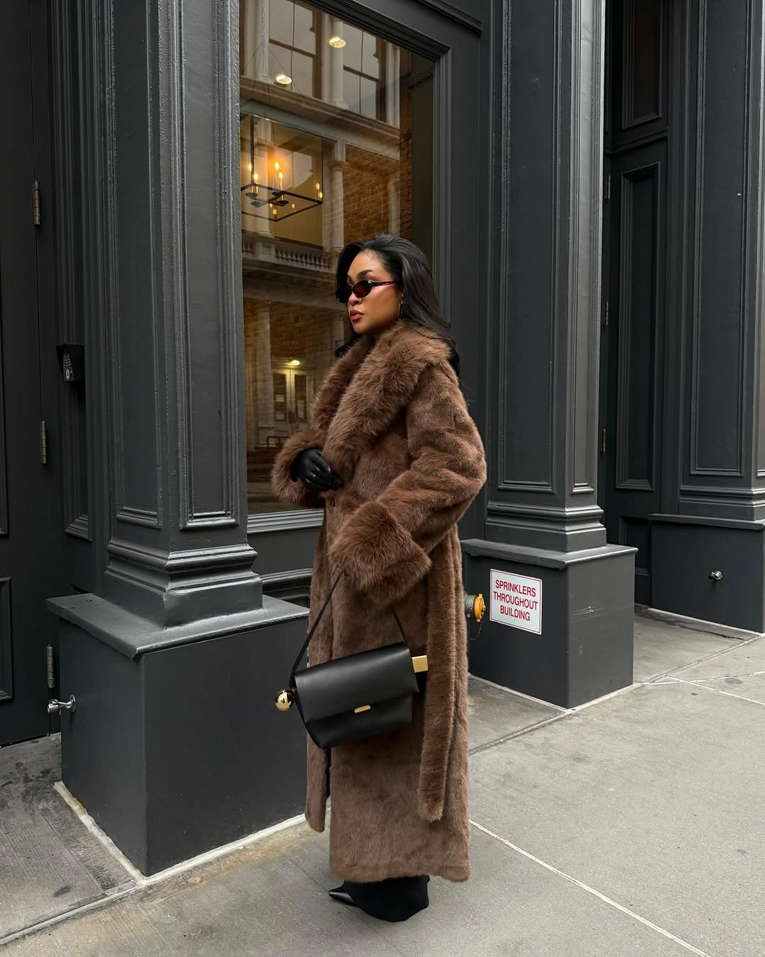Long chocolate-brown fuzzy coat with black gloves and shoulder bag